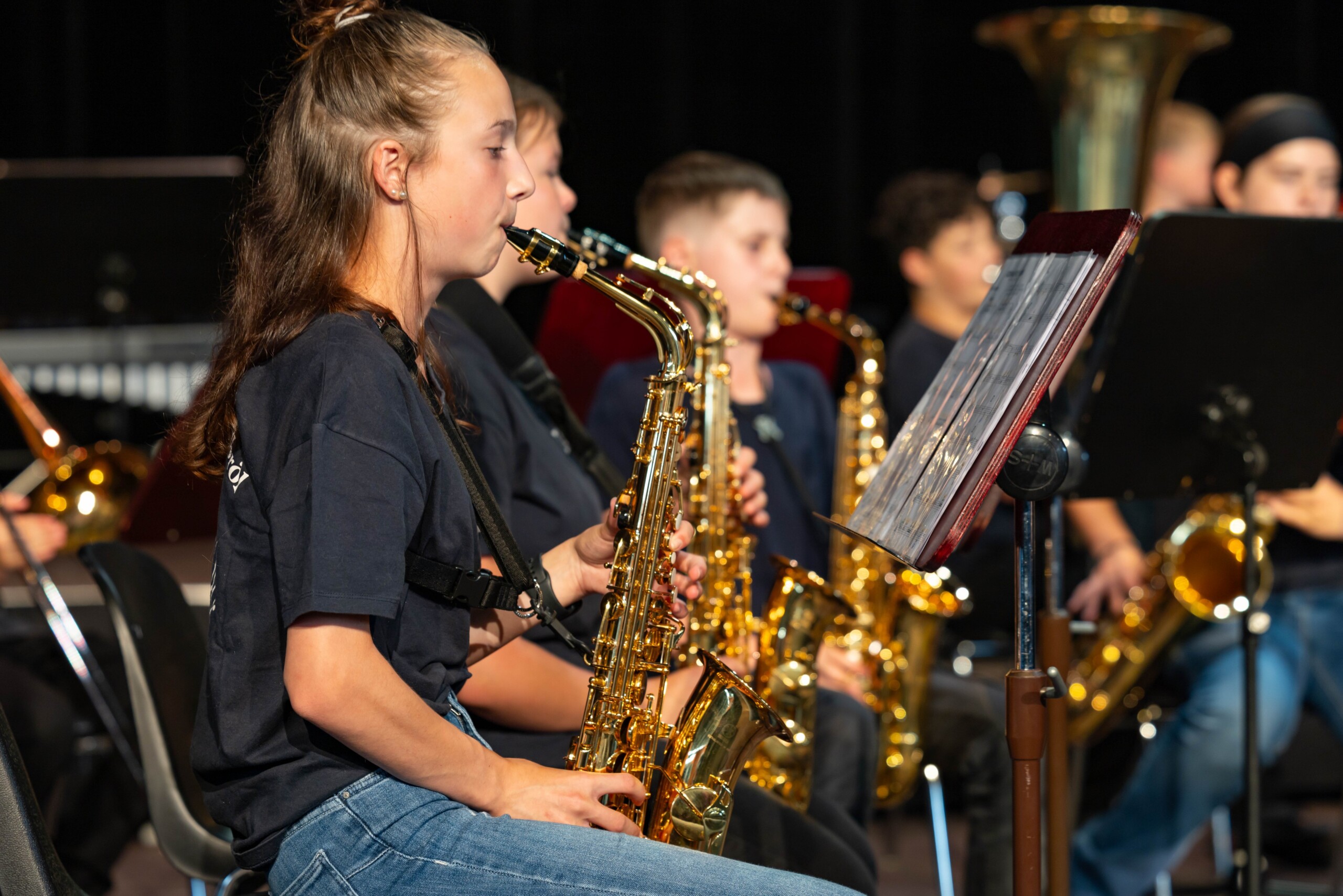 Nahaufnahme einer Schülerin am Altsaxophon – im Vordergrund das goldene Instrument, im Hintergrund das harmonisch agierende Bläserensemble der Klasse.