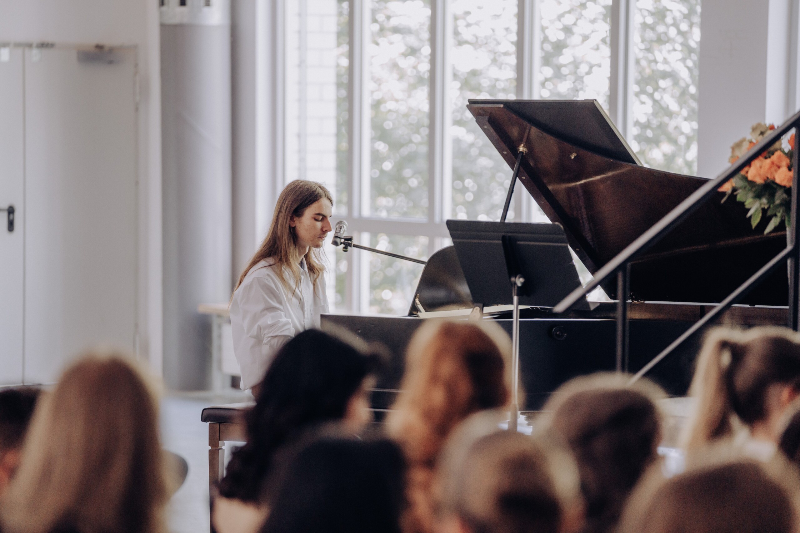Jakob Walther aus der Q1 spielt am Flügel ein klassisches Klavierstück – das Publikum im Vordergrund lauscht aufmerksam seinem Vortrag.