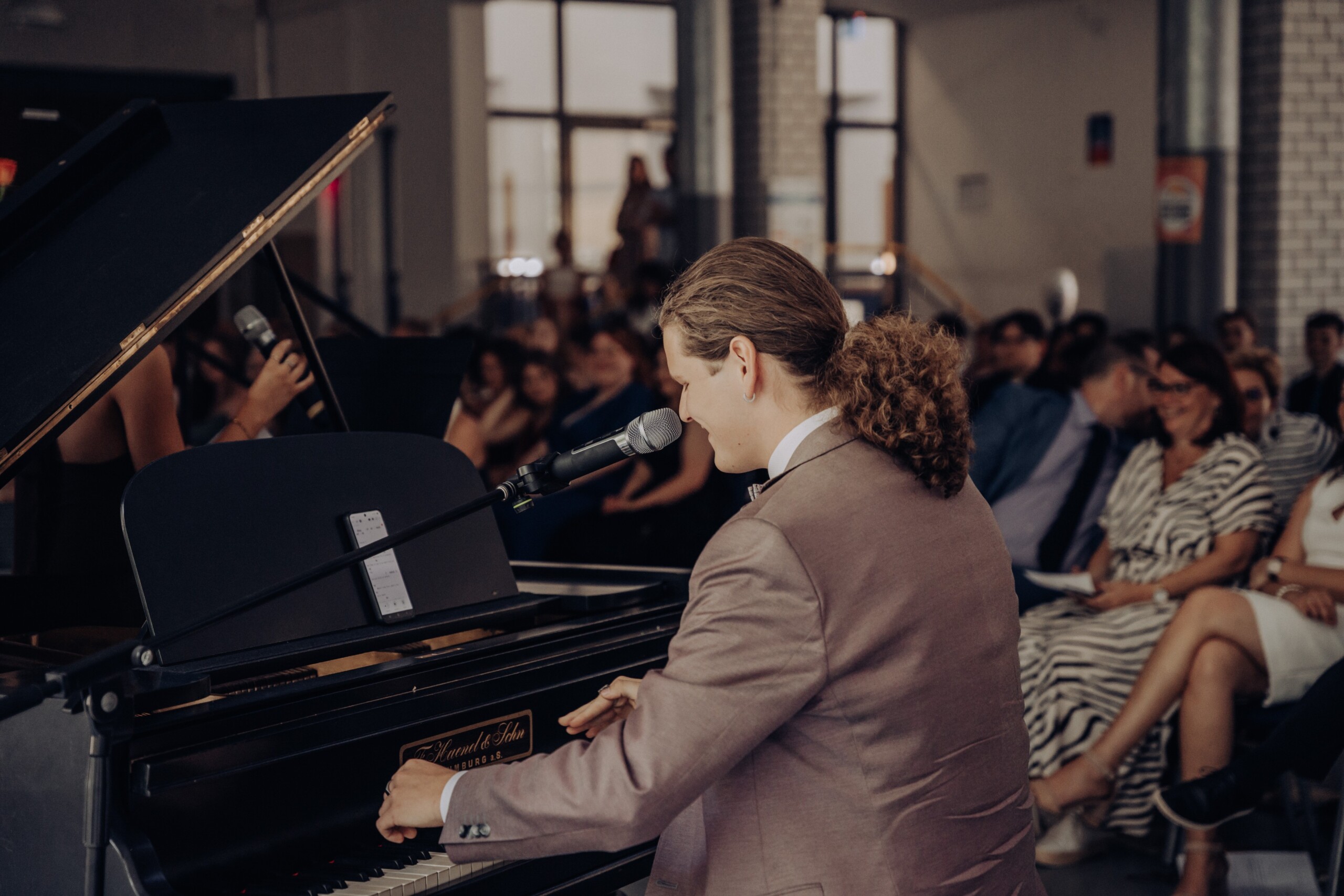 Abiturient Tom Ohlig am Klavier, während er gemeinsam mit Cennet Heil ein Musikstück aufführt – im Hintergrund ist das Publikum sichtbar.