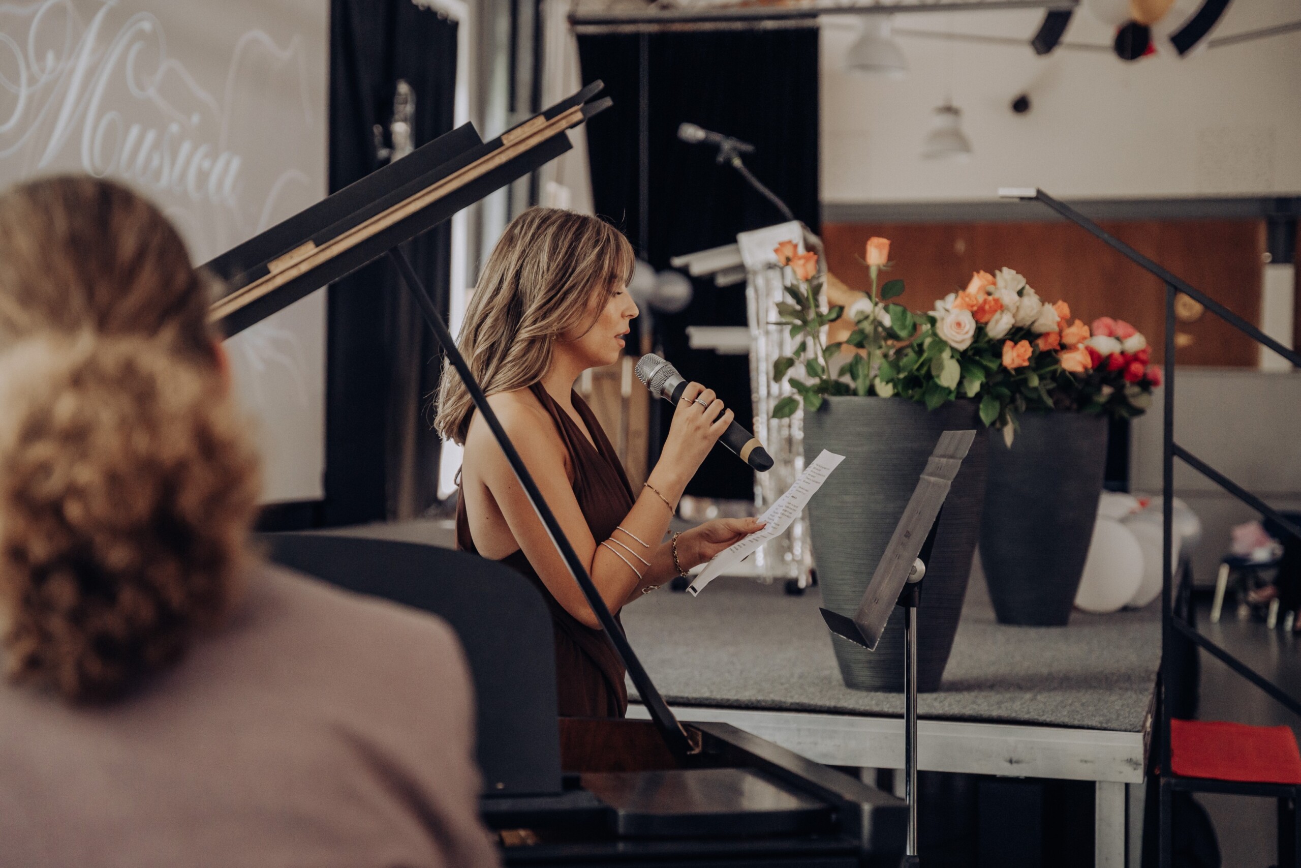 Abiturientin Cennet Heil singt in ein Mikrofon, während sie gemeinsam mit Tom Ohlig auf der Bühne musiziert – neben ihr ein Blumenarrangement und das Rednerpult.