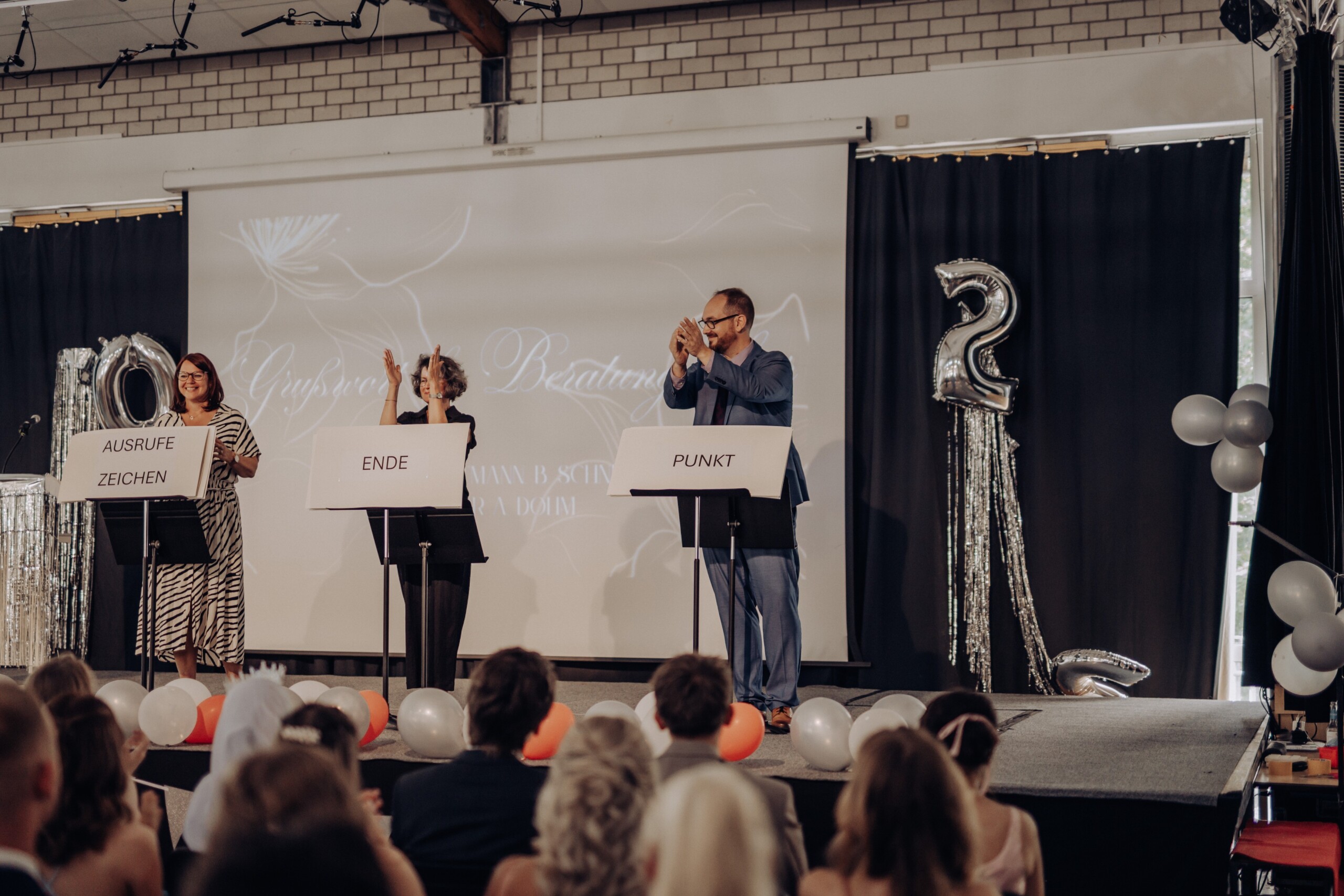Die drei Beratungslehrkräfte präsentieren ihre kreative „stumme Rede“ – mit Pappschilden beschriftet als „Ausrufezeichen“, „Ende“ und „Punkt“, begleitet von Applaus aus dem Publikum.