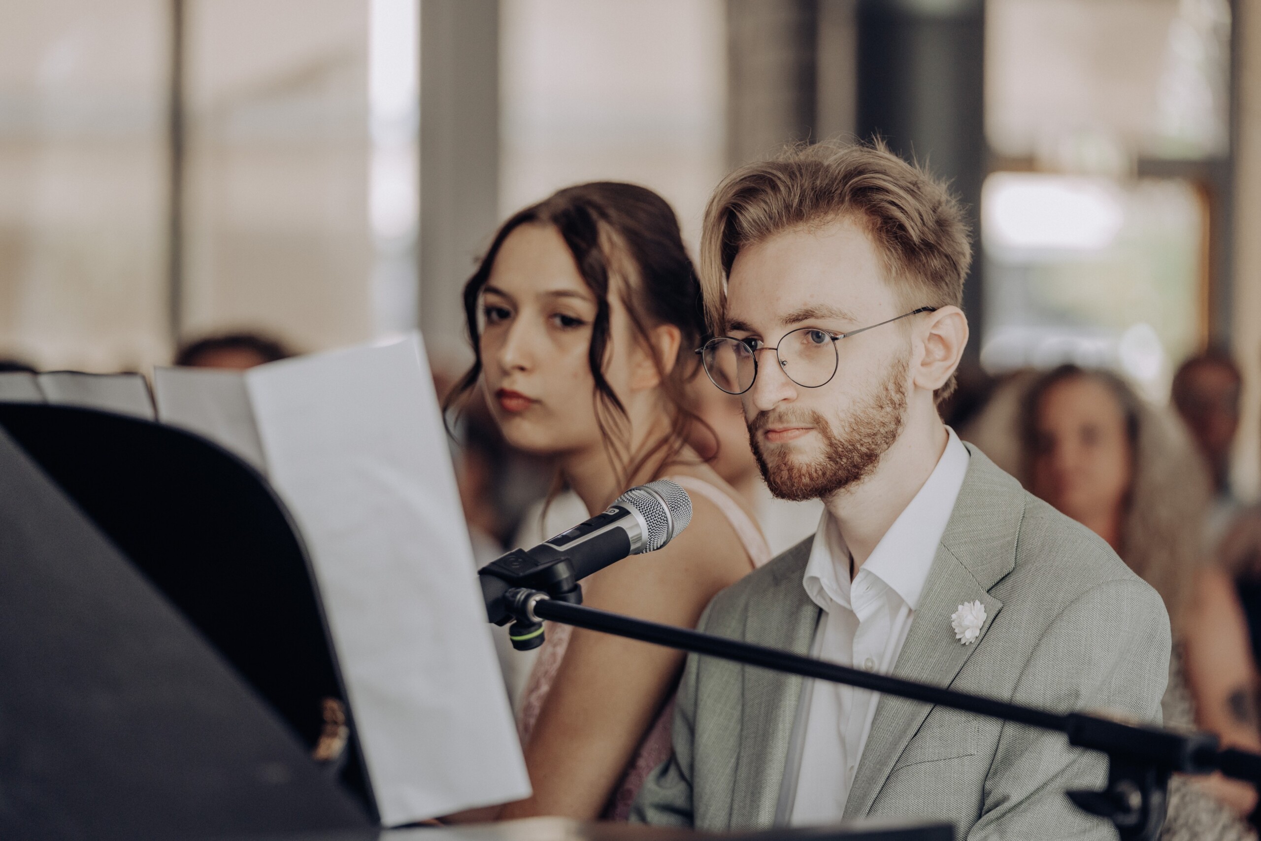 Abiturient Simon Rothe sitzt am Klavier und singt gemeinsam mit Marie Wagener – beide blicken konzentriert in Richtung Publikum, das im Hintergrund zu erkennen ist.