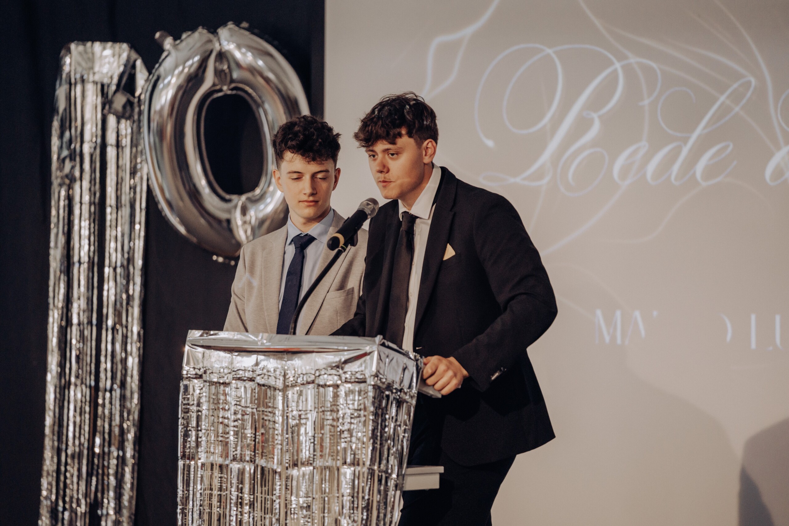 Marko Luketic und Mika Schneider halten als Abiturienten gemeinsam die Abschlussrede – sie stehen nebeneinander am Rednerpult vor einer projizierten Schrift im Hintergrund.