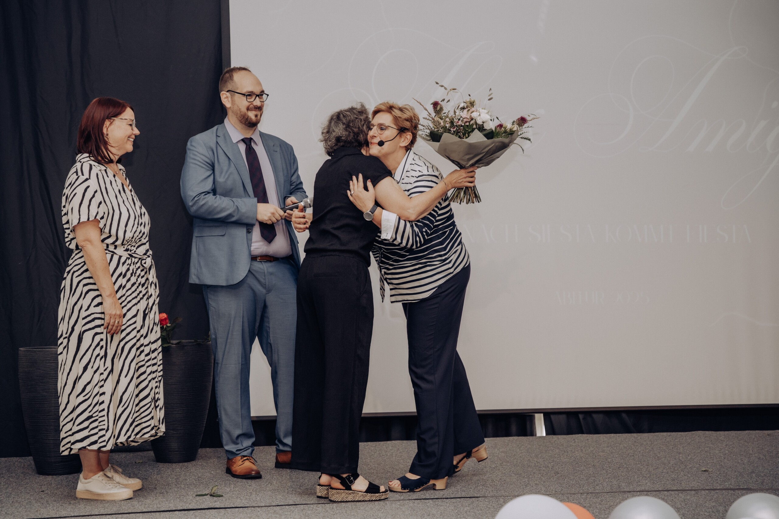 Oberstufenleiterin Ute Gick erhält zum Abschluss der Abiturfeier einen großen Blumenstrauß und eine herzliche Umarmung von ihrem Beratungsteam.