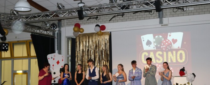 Die gleiche Gruppe wird erneut auf der Bühne gezeigt, diesmal applaudieren sie gemeinsam – ein Moment der Wertschätzung und Freude.