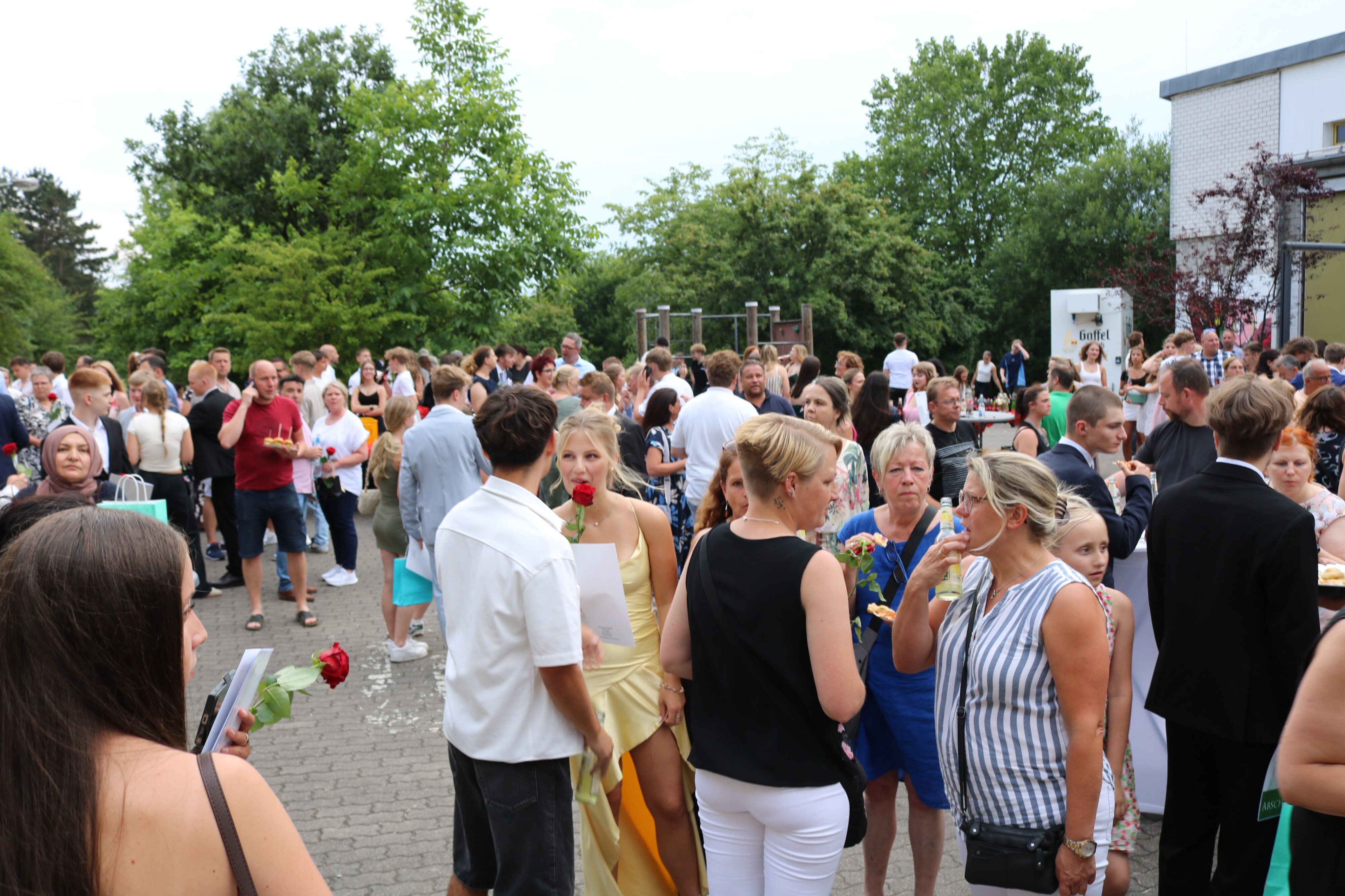 Feierliche Stimmung auf dem Schulhof: Hunderte Gäste und Absolvent:innen versammeln sich bei sommerlichem Wetter zum geselligen Ausklang der Abschlussfeier.