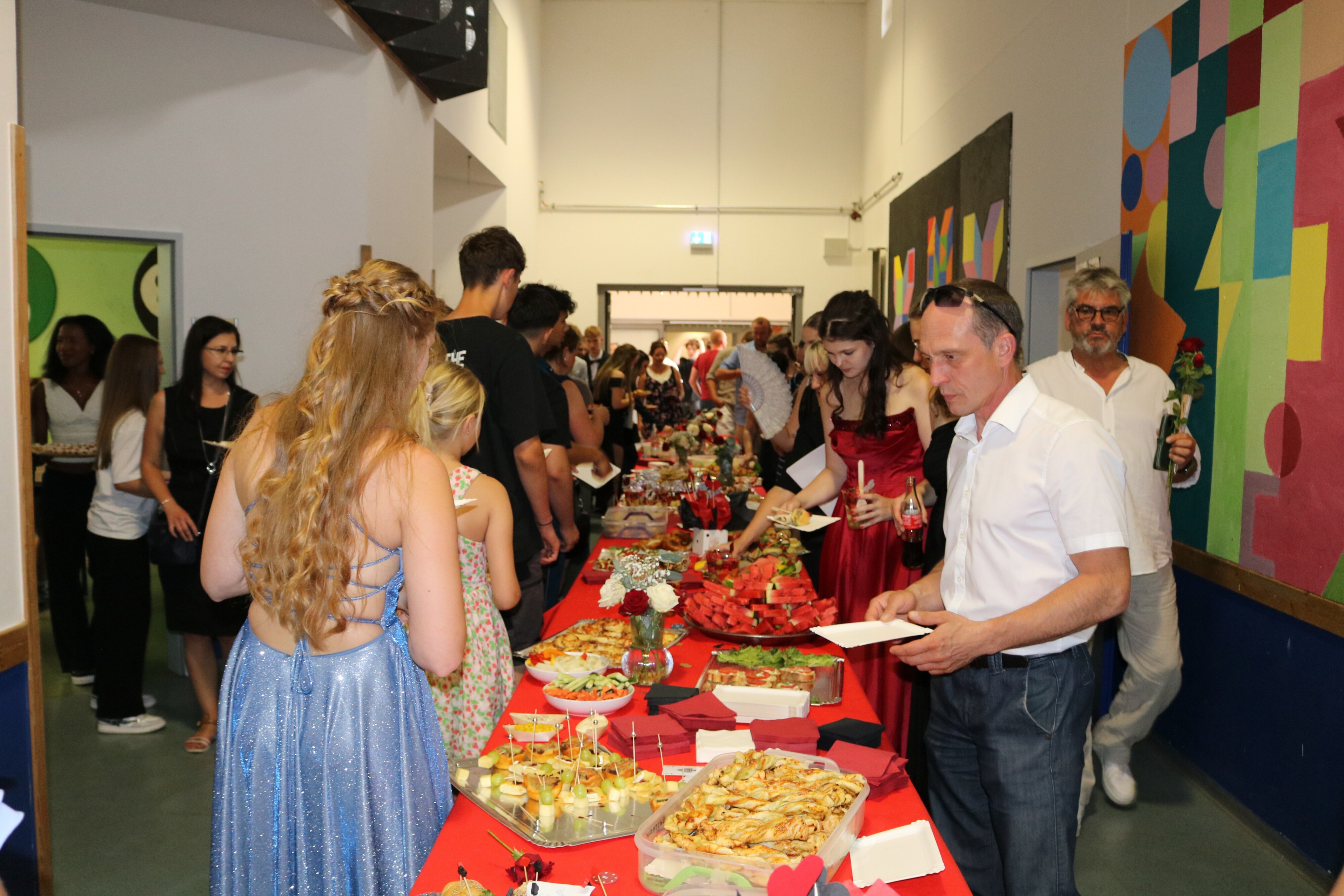 Blick auf das reichhaltige Buffet im Schulflur – Gäste und Absolvent:innen bedienen sich an einer langen Tafel mit süßen und herzhaften Snacks.