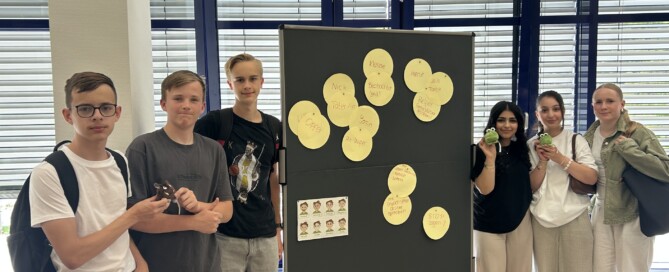 Die Gruppe der Social Media Scouts steht vor einer Präsentationstafel mit Stichworten zum Thema Medienkompetenz; sie halten kleine Maskottchen in den Händen.