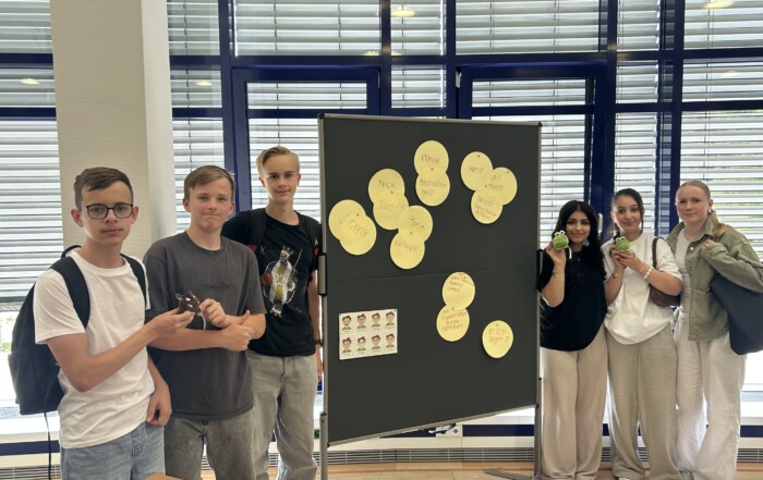 Die Gruppe der Social Media Scouts steht vor einer Präsentationstafel mit Stichworten zum Thema Medienkompetenz; sie halten kleine Maskottchen in den Händen.