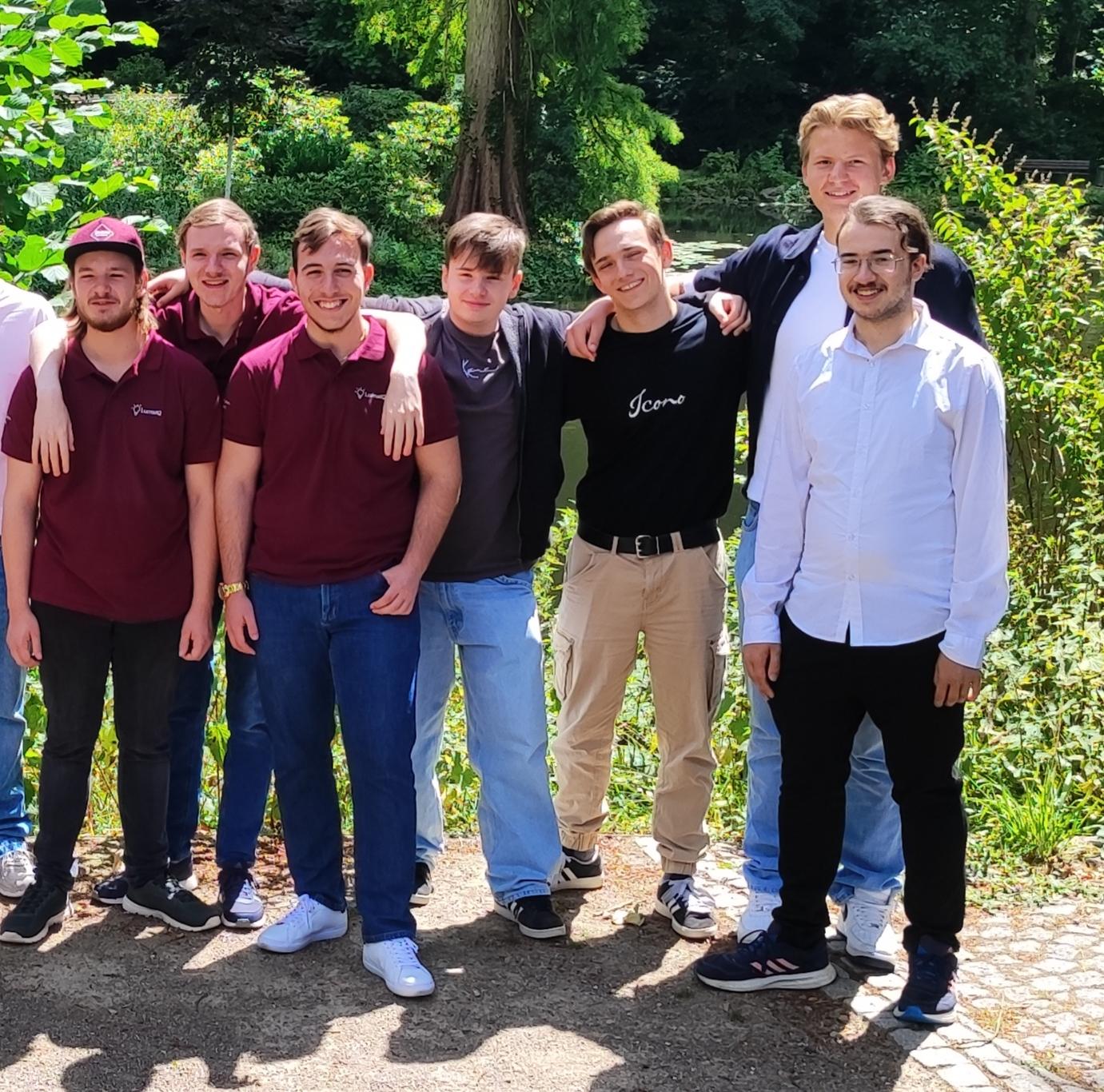 Gruppenfoto beider Teams der Gesamtschule Waldbröl vor grüner Kulisse im Schlosspark Eller: Die Jugendlichen stehen entspannt nebeneinander, einige mit verschränkten Armen, andere mit lachendem Blick zur Kamera.