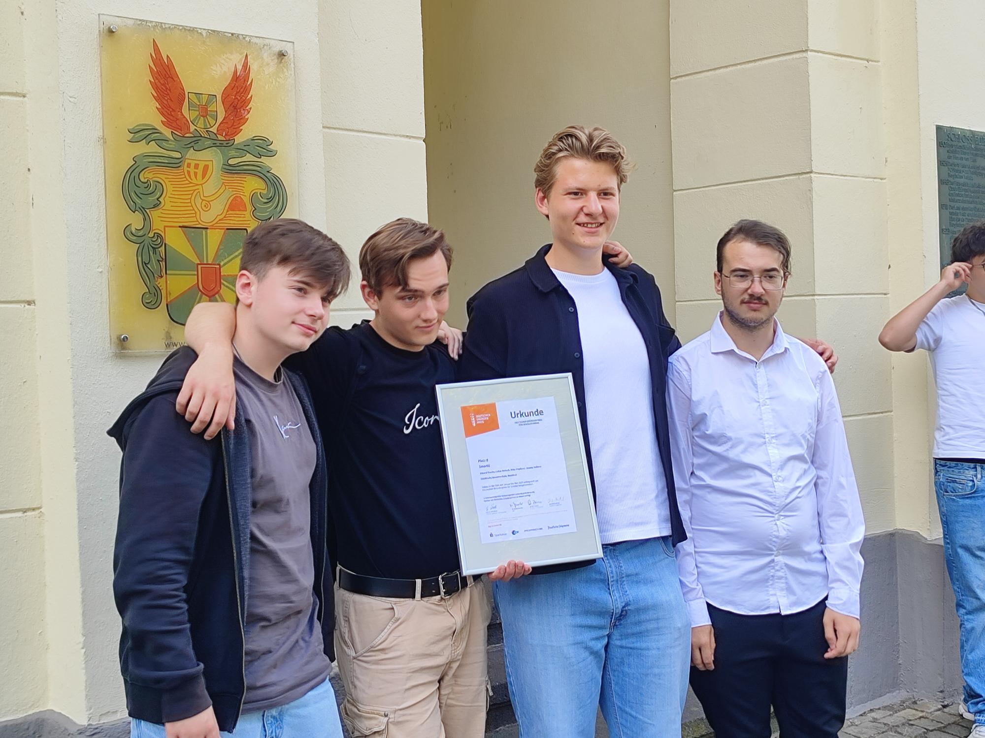 Vier Mitglieder des Teams SmartG vor dem Eingang von Schloss Eller: Ein Teammitglied hält stolz die gerahmte Urkunde für den 8. Platz, im Hintergrund ist ein Wappen zu sehen.