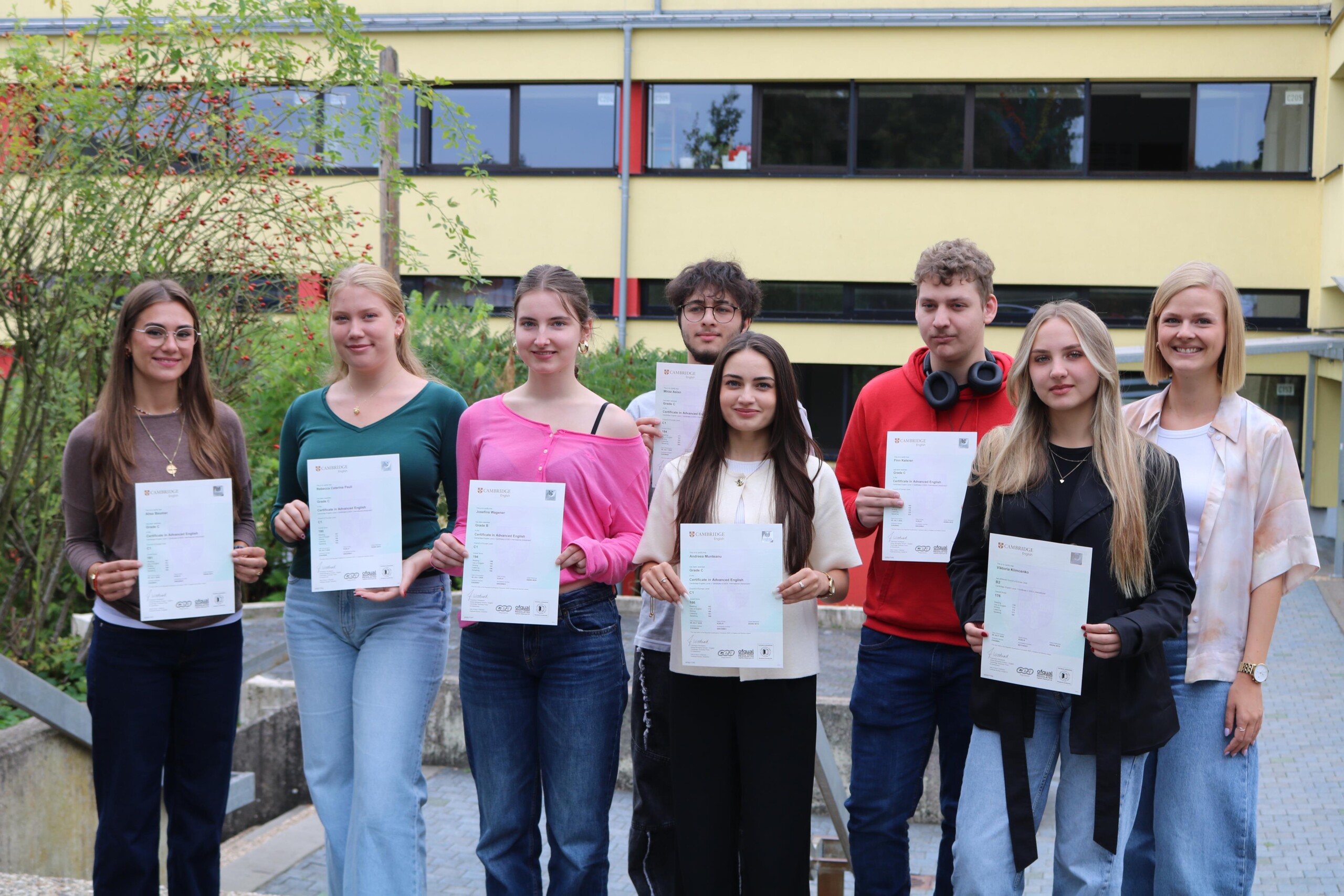 Acht Schüler:innen des Cambridge-Projektkurses der Gesamtschule Waldbröl halten stolz ihre Cambridge-Zertifikate in den Händen, gemeinsam mit Kursleiterin Lisa Dornseifer.