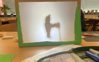 Ein selbstgebautes Schattentheater steht auf einem Tisch, dahinter ist die Silhouette einer Figur zu erkennen.