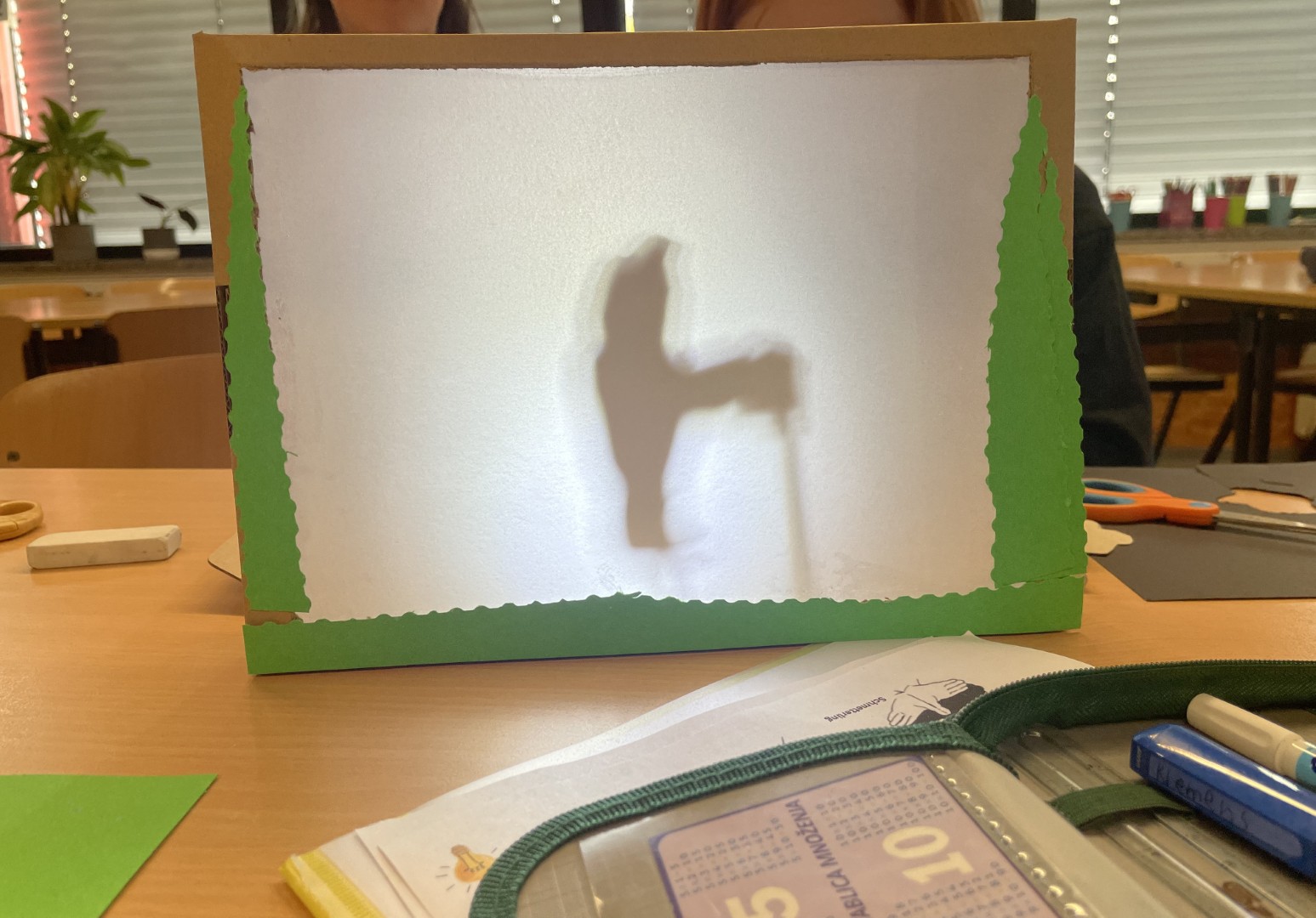 Ein selbstgebautes Schattentheater steht auf einem Tisch, dahinter ist die Silhouette einer Figur zu erkennen.