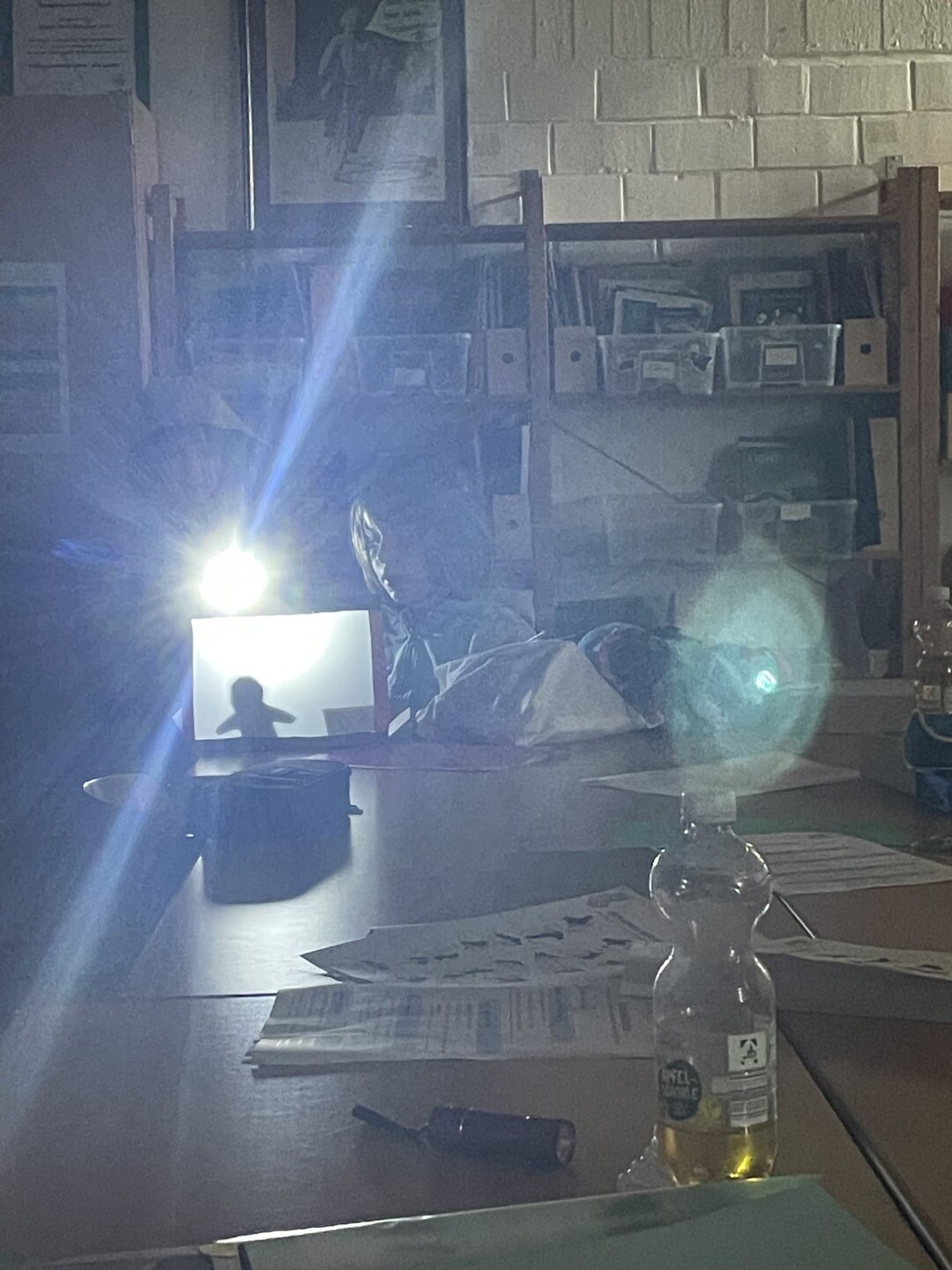 Ein heller Lichtstrahl eines Projektors fällt in einem dunklen Raum auf eine kleine Schattenbühne, auf der die Silhouette einer Figur zu sehen ist.