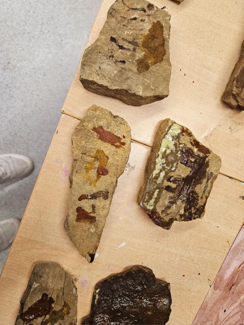 Mehrere bemalte Steine mit erdfarbenen Motiven liegen auf einem Tisch – Ergebnisse aus dem Workshop Höhlenmalerei.
