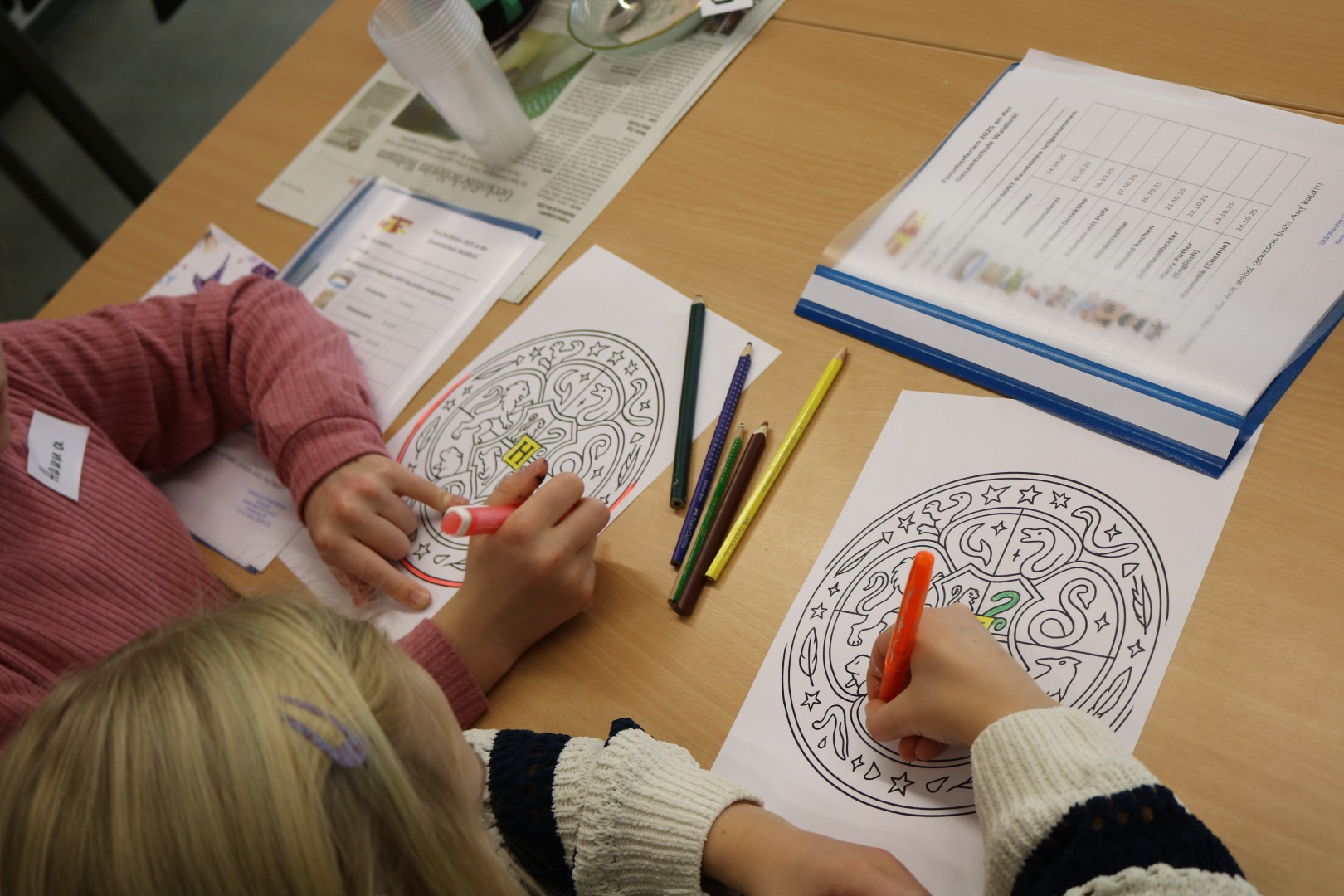 Zwei Kinder malen konzentriert mit Buntstiften ein Mandala mit Hogwarts-Motiv aus.
