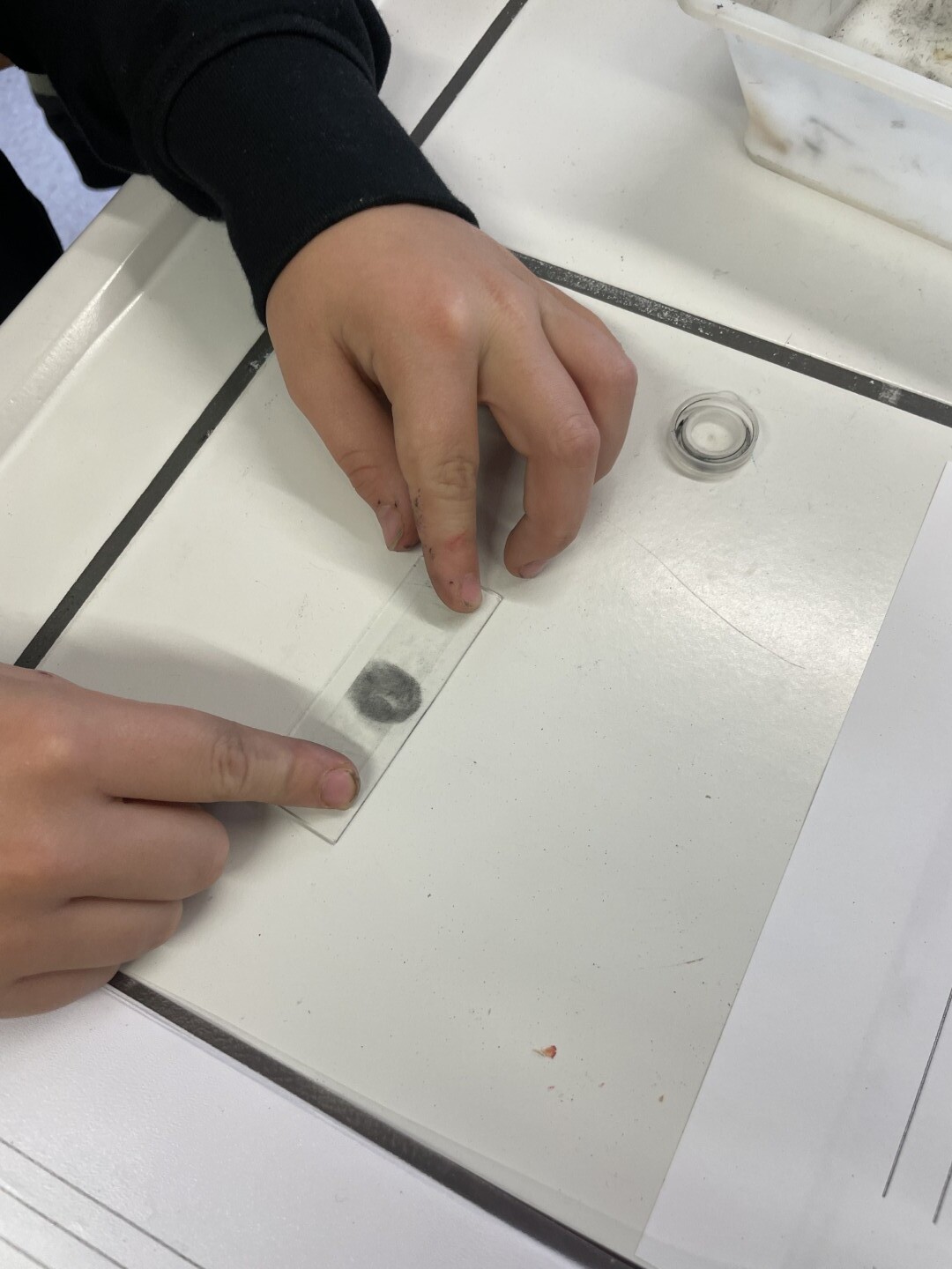 Nahaufnahme zweier Kinderhände, die einen Fingerabdruck auf einem Objektträger fixieren.