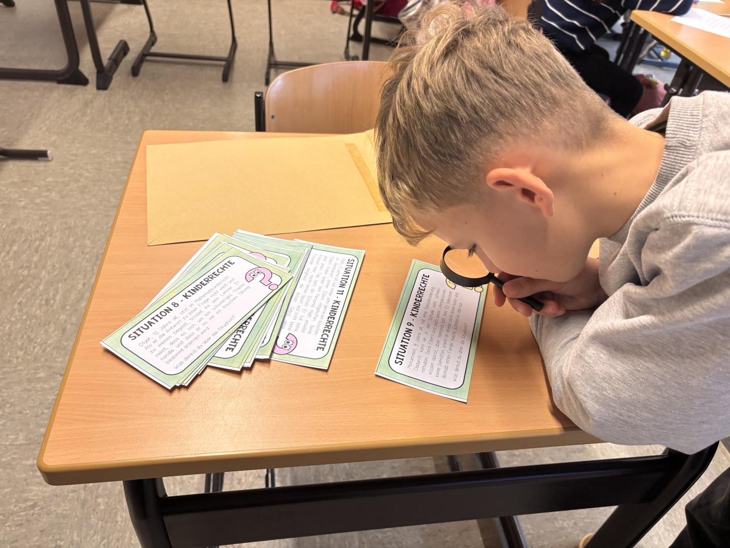 Ein Junge liest eine Karte zum Thema Kinderrechte durch eine Lupe.