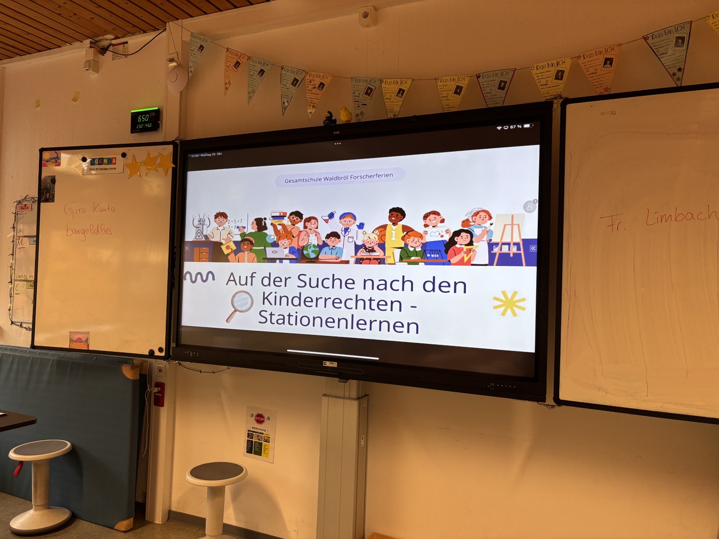 Ein interaktives Whiteboard zeigt die Präsentation „Auf der Suche nach den Kinderrechten – Stationenlernen“ in einem Klassenraum.