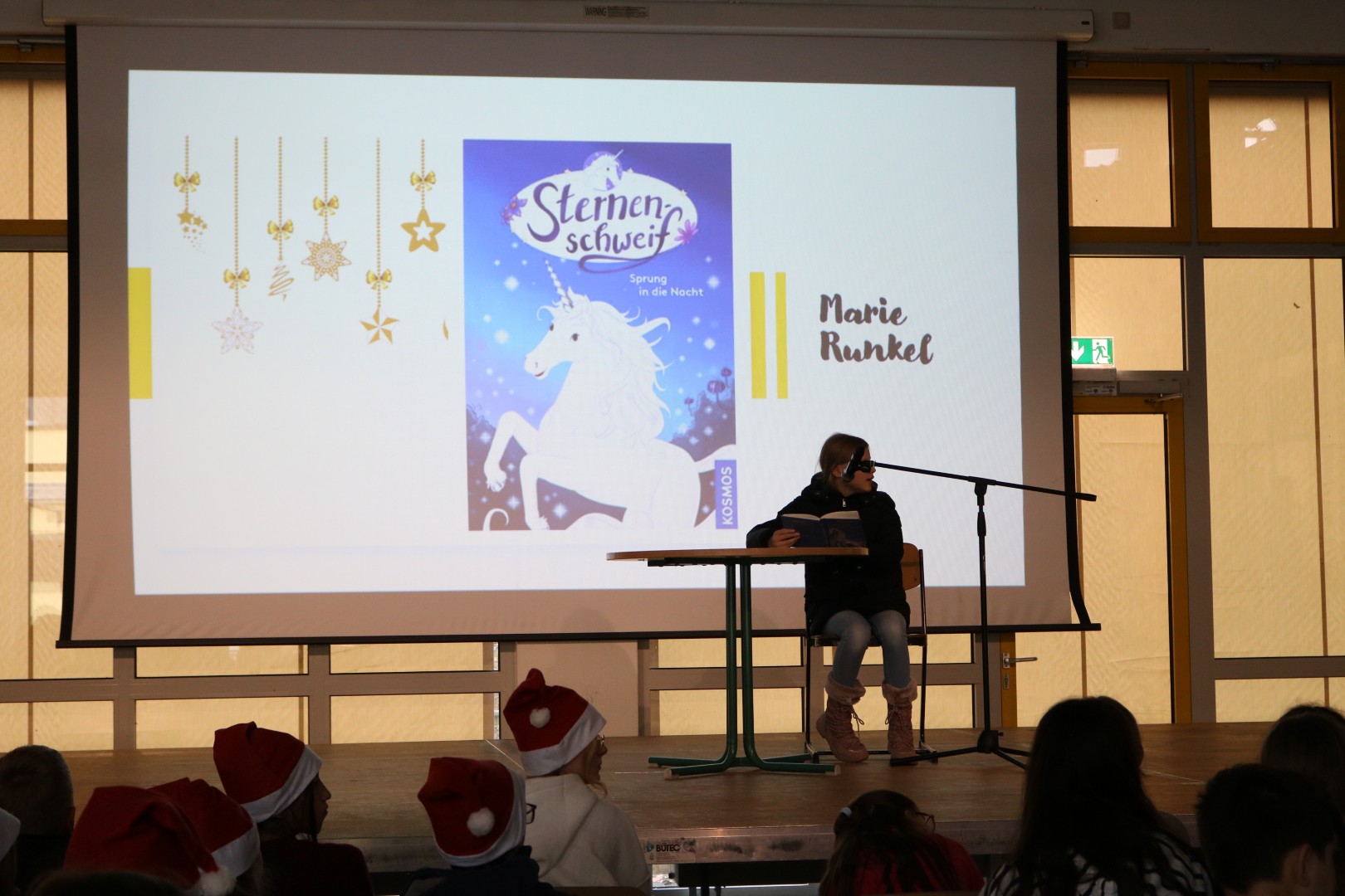 Schülerin liest am Mikrofon; im Hintergrund ist das Buchcover „Sternenschweif – Sprung in die Nacht“ auf der Leinwand zu erkennen.