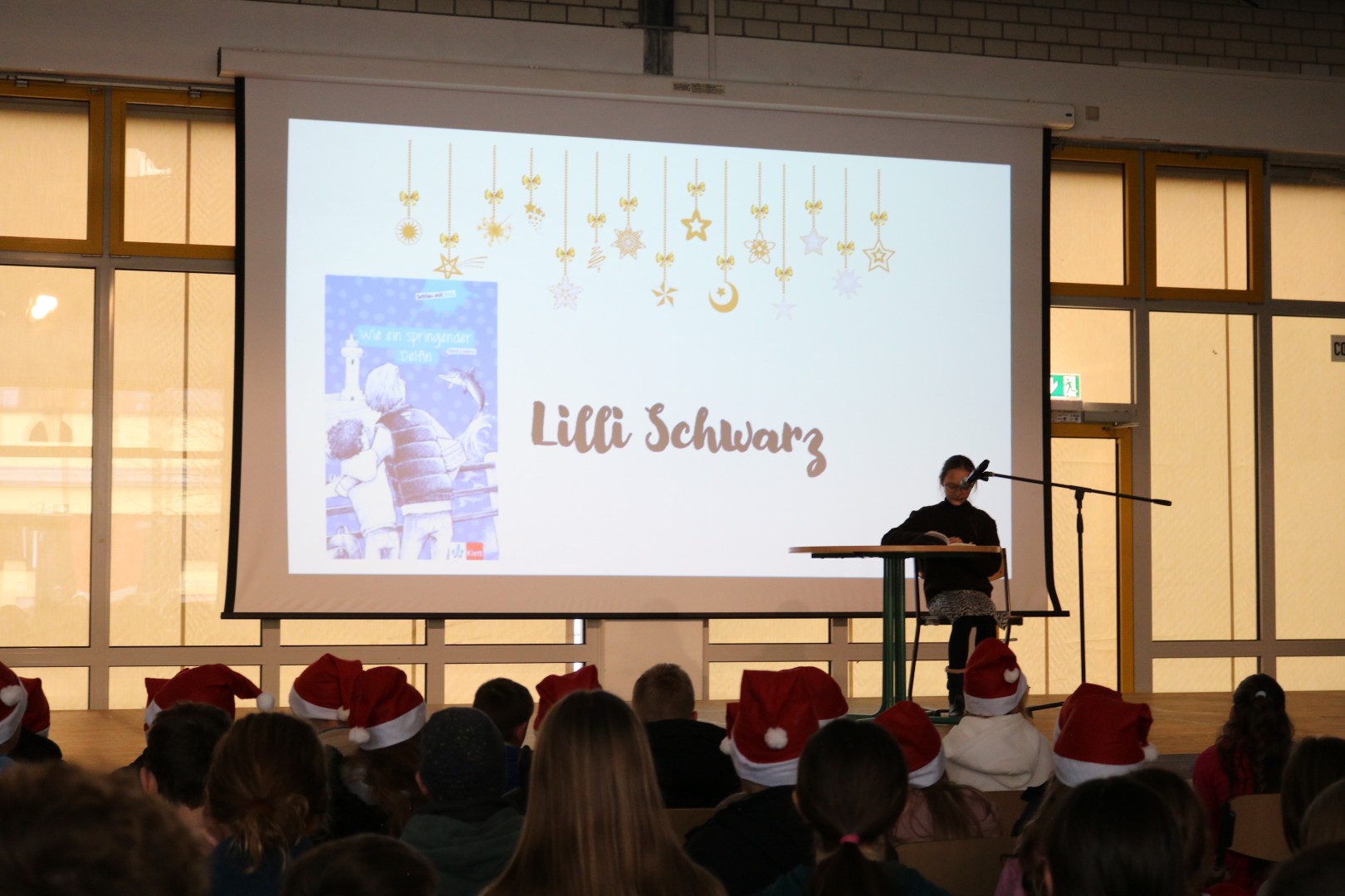 Schülerin liest konzentriert an einem Tisch; im Hintergrund wird das Buchcover „Wie ein springender Delfin“ projiziert.