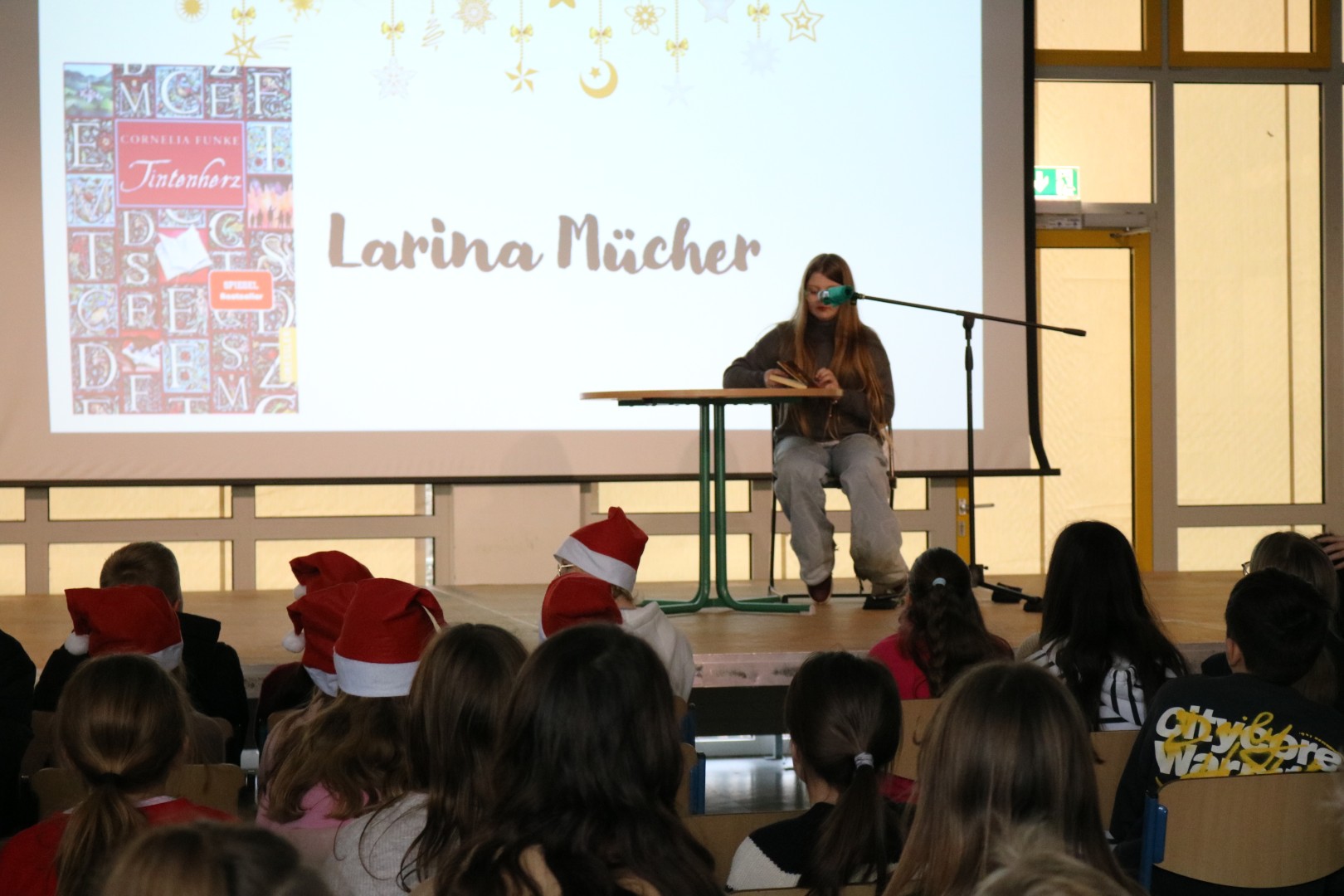 Schülerin liest aus „Tintenherz“ vor, dessen Buchcover deutlich auf der Projektionsfläche angezeigt wird.