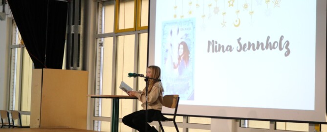 Schülerin liest an einem Stehtisch aus einem Buch; auf der Leinwand ist „Pferdeflüsterer Mädchen – Rubys Entscheidung“ zu sehen.