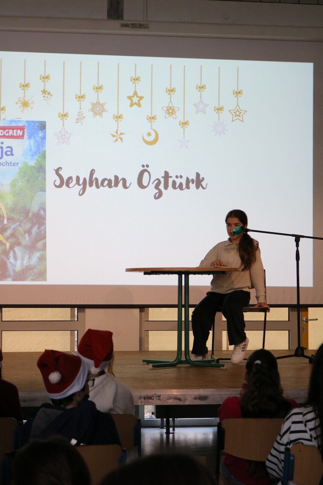 Schülerin liest am Tisch, im Hintergrund das Buchcover „Ronja Räubertochter“ auf der Projektionsfläche.