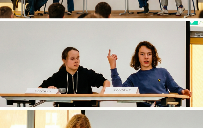Collage aus drei Bildern einer Debattenveranstaltung auf einer Bühne vor weißem Hintergrund. Das obere Bild zeigt die Gesamtszene mit zwei Zweierteams an Tischen; ein:e Teilnehmer:in auf der rechten Seite spricht gestikulierend in ein Mikrofon. Die unteren Detailaufnahmen zeigen das Pro-Team beim konzentrierten Mitschreiben sowie das Kontra-Team während eines Redebeitrags mit erhobenem Zeigefinger.