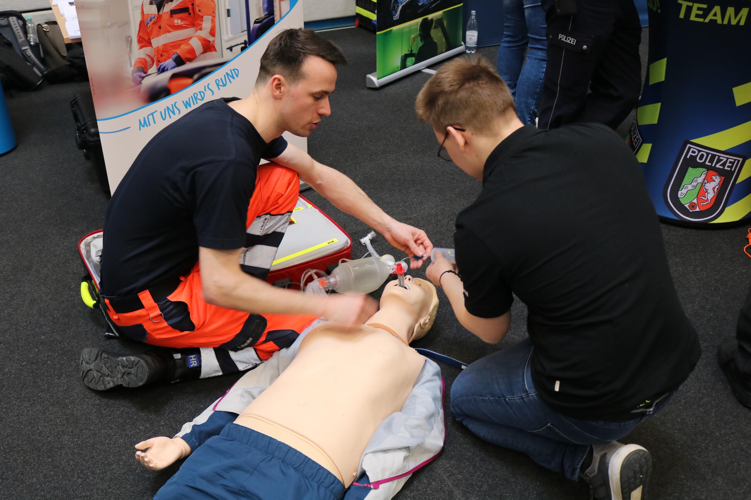 Schüler:innen erproben gemeinsam mit einem Rettungssanitäter eine Reanimationssituation an einer Übungspuppe. Die konzentrierte Atmosphäre verdeutlicht den praxisnahen Zugang zur Berufsorientierung.