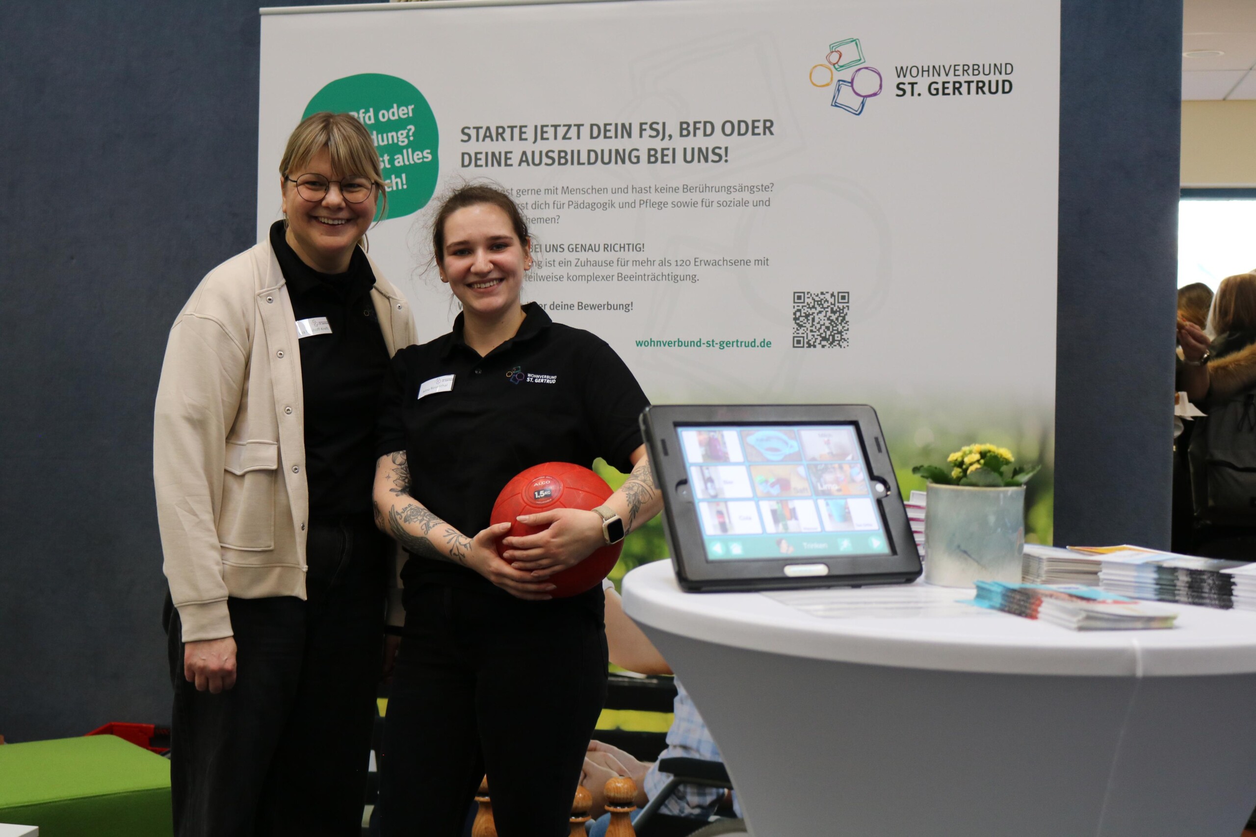 Zwei Vertreterinnen eines sozialen Trägers stehen an einem Messestand und informieren über Freiwilligendienste und Ausbildungswege. Der offene Stand lädt zu Gesprächen in persönlicher Atmosphäre ein.