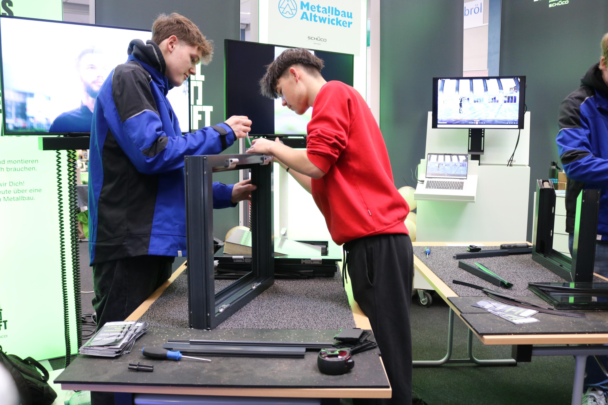 Zwei Schüler montieren gemeinsam ein Bauteil an einem Messestand eines Metallbauunternehmens. Die konzentrierte Zusammenarbeit unterstreicht den handlungsorientierten Charakter der Messe.