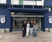 Vier Schülerinnen der Gesamtschule stehen vor dem Eingang der Partnerschule I.E.S. Santa Catalina de Alejandría in Jaén. Über dem Eingang ist der Schulname auf einem Schild zu sehen.