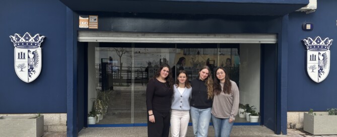 Vier Schülerinnen der Gesamtschule stehen vor dem Eingang der Partnerschule I.E.S. Santa Catalina de Alejandría in Jaén. Über dem Eingang ist der Schulname auf einem Schild zu sehen.