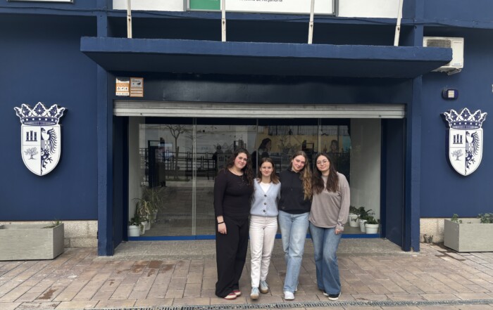 Vier Schülerinnen der Gesamtschule stehen vor dem Eingang der Partnerschule I.E.S. Santa Catalina de Alejandría in Jaén. Über dem Eingang ist der Schulname auf einem Schild zu sehen.