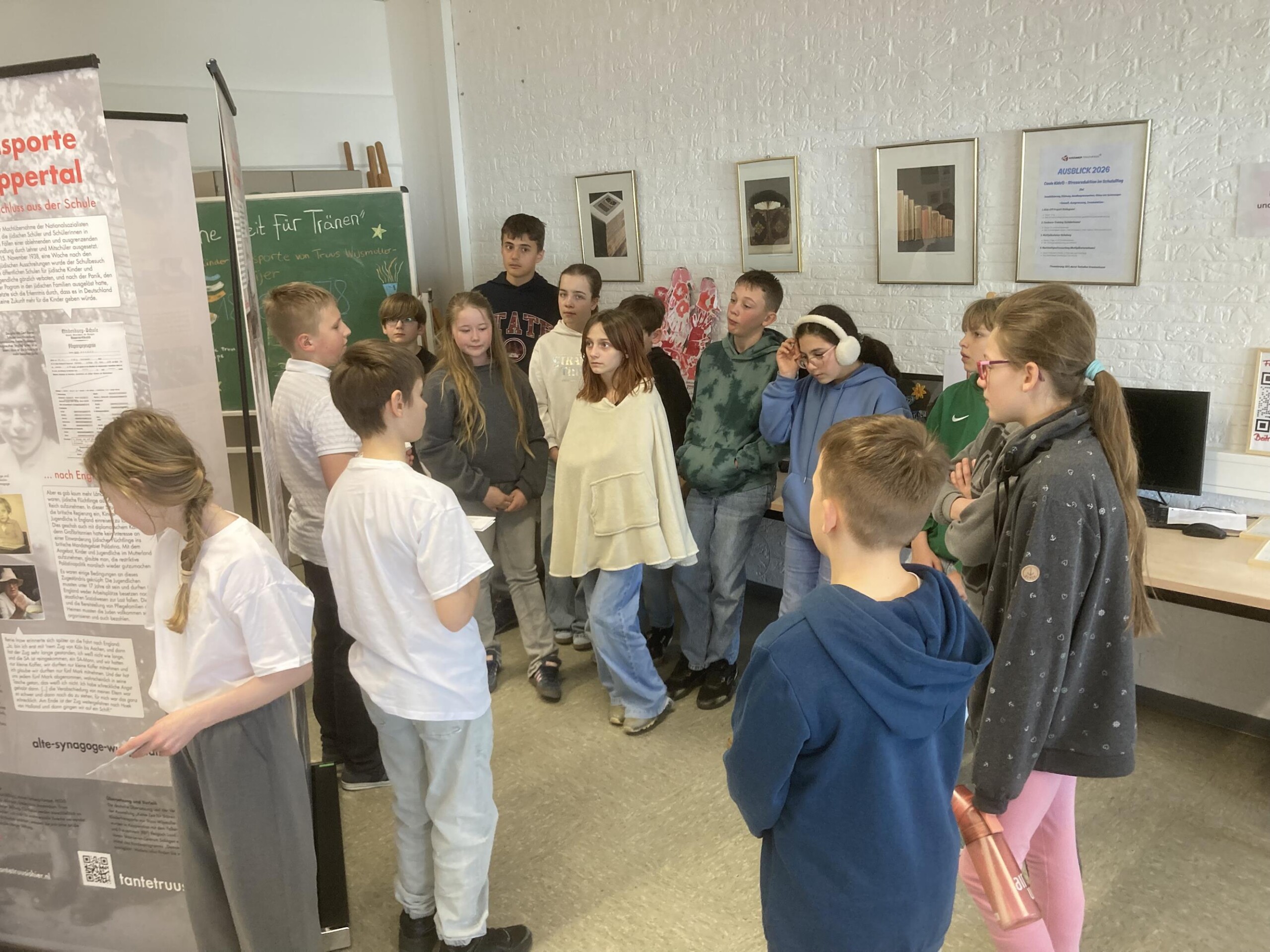Schüler:innen stehen in einer Gruppe vor Ausstellungstafeln zur Wanderausstellung „Keine Zeit für Tränen“ und hören einer Präsentation zu.