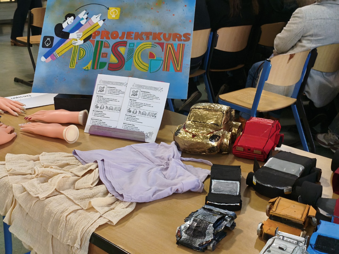 Projektkurs „Design“ präsentiert praktische Arbeiten wie Modelle und Materialien auf einem Ausstellungstisch.