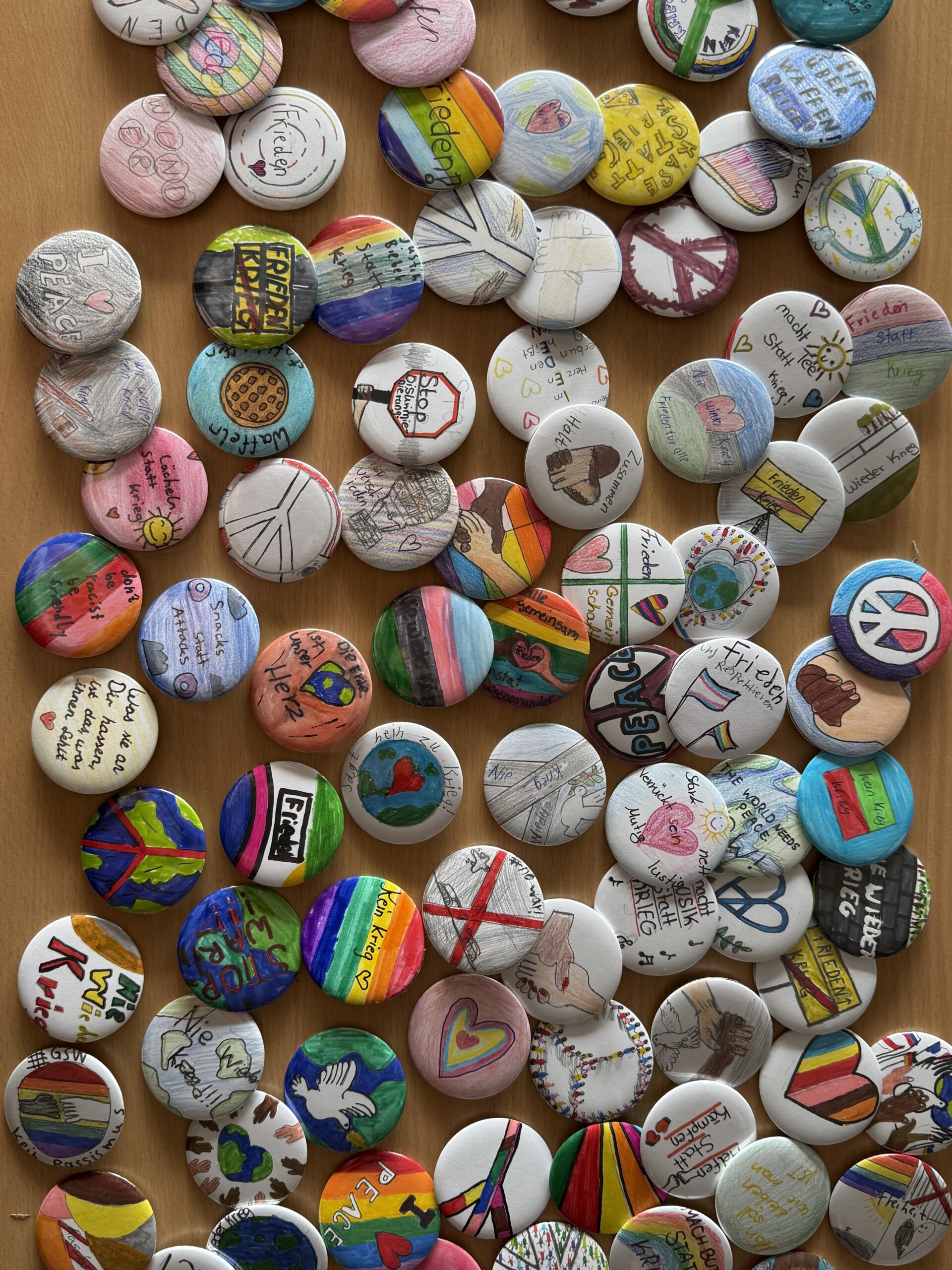 Viele selbst gestaltete Buttons mit Zeichnungen und Botschaften zu Frieden, Vielfalt und Zusammenhalt liegen auf einem Tisch.