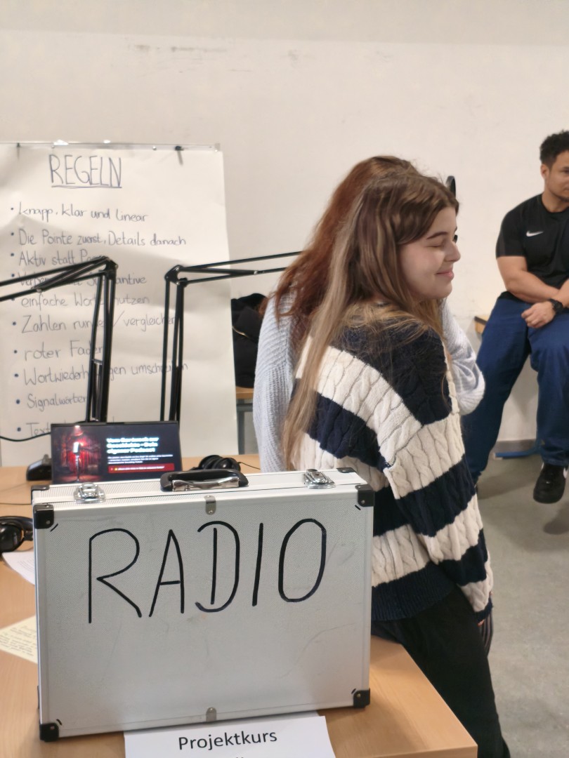Schülerin stellt den Projektkurs „Radio“ vor; im Hintergrund sind Stichpunkte zur Arbeitsweise sichtbar.