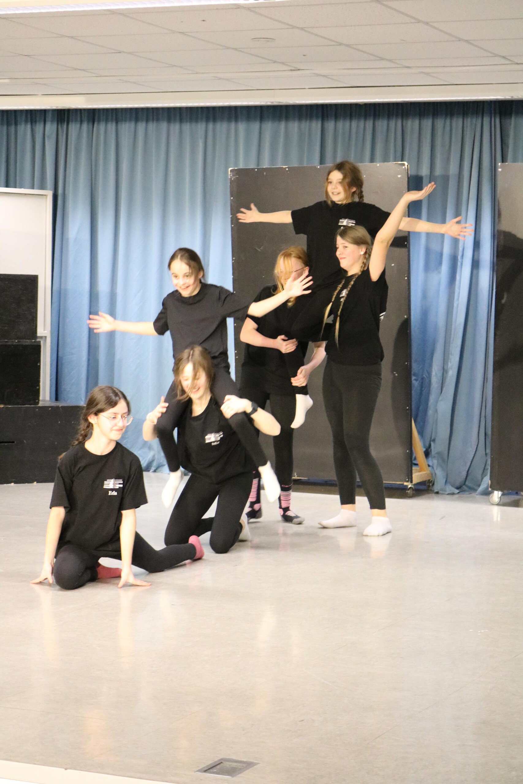 Die Turngruppe der Klasse 6d beendet eine Formation ihrer Tanzchoreografie mit ausgebreiteten Armen auf der Bühne.