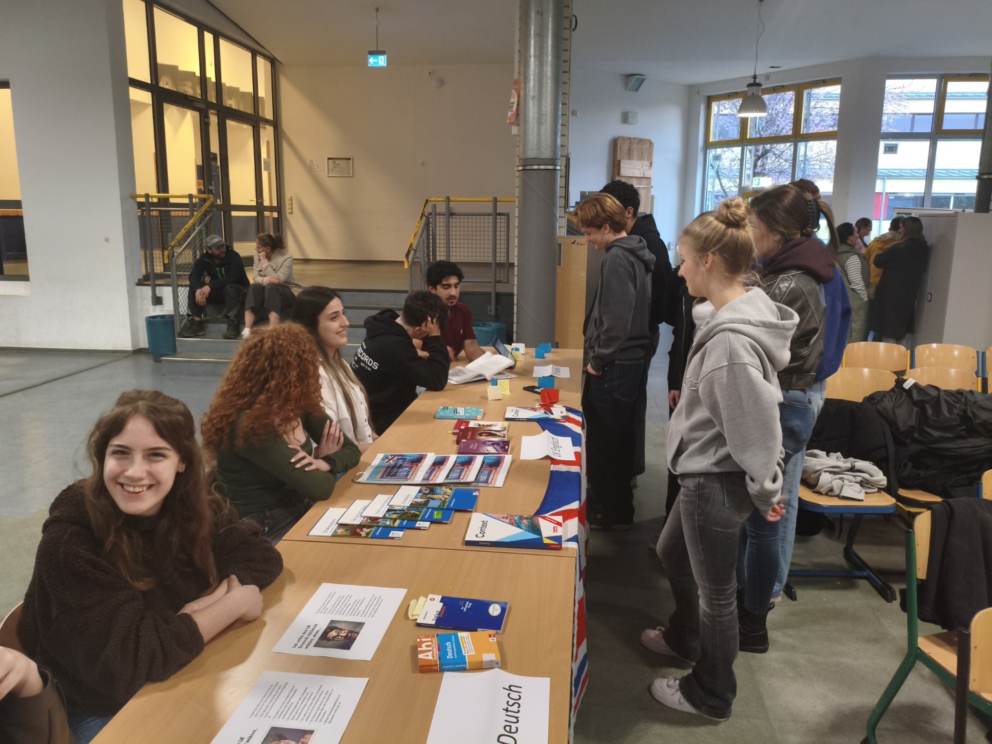 Schüler:innen der Q1 beraten an mehreren Ständen zu Kursangeboten; entlang einer langen Tischreihe kommen sie mit den Schüler:innen der EF ins Gespräch.