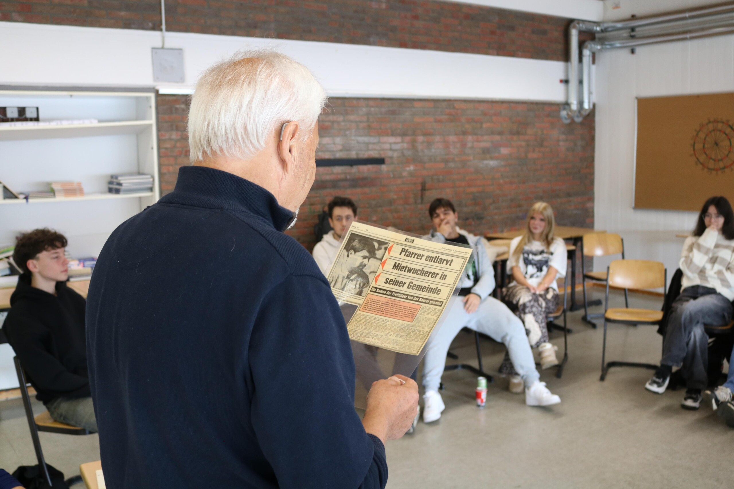 Michael Höhn zeigt Schüler:innen in einem Stuhlkreis ein historisches Dokument und spricht über seine Erfahrungen aus Friedens- und Bildungsarbeit.